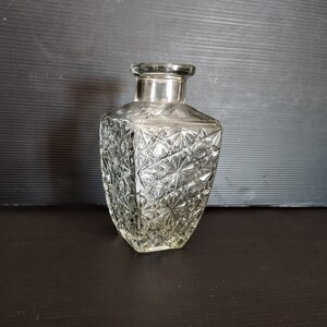 Puede incluir: Una decantador de vidrio transparente con un patrón geométrico texturizado. La decantador tiene una parte superior plateada.