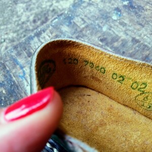 Pode incluir: Close-up do interior de um sapato de couro marrom com uma etiqueta verde que diz "120 7060 02-02".