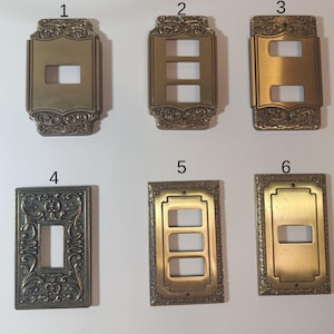 Op de afbeelding: Een verzameling van zes antieke messing lichtschakelaar covers. De covers hebben sierlijke, reliëf ontwerpen en verschillende configuraties voor enkele, dubbele en drievoudige schakelaars. Het metaal heeft een warme, verouderde patina.