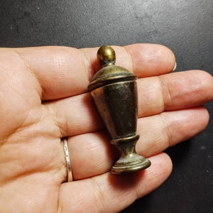May include: A small, antique-looking, gold-toned metal finial with a rounded top and a fluted base.