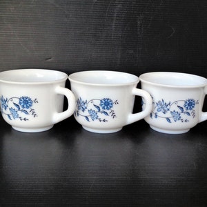 May include: Three white ceramic mugs with blue floral designs. The mugs have a simple, classic shape and are perfect for everyday use.