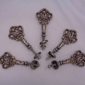 May include: Six antique silver key-shaped cabinet knobs with ornate details. Each knob features a decorative keyhole design and a screw-on mounting.
