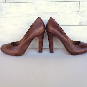 May include: A pair of brown leather heeled pumps with a rounded toe.