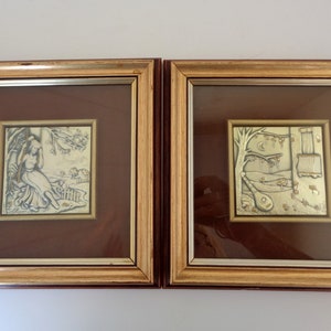 May include: Two framed silver embossed artwork pieces. The artwork on the left depicts a woman sitting in a field with a tree behind her. The artwork on the right depicts a scene with a tree, a crescent moon, a window, and a lute.