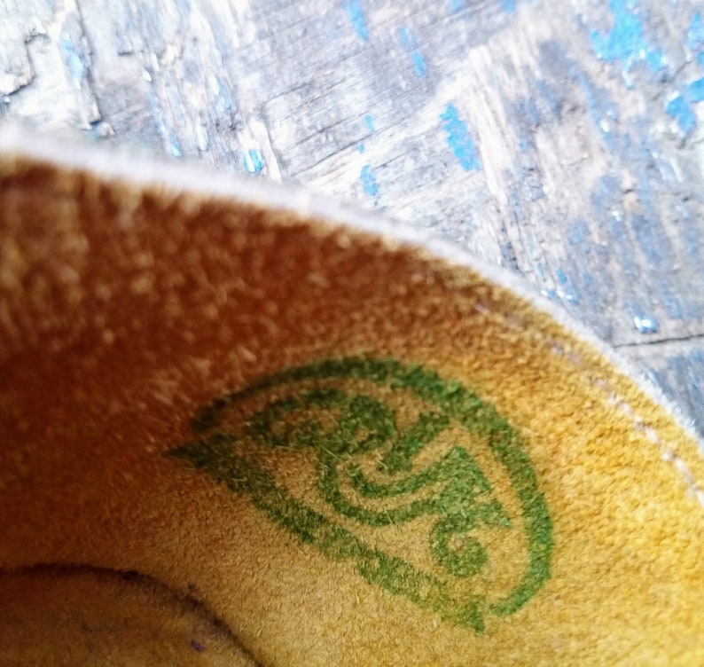 Pode incluir: Close-up do interior de um sapato com um logotipo verde na palmilha. O logotipo &eacute; um design de espiral estilizado.