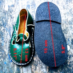 Pode incluir: Sapatos de couro verde para crian&ccedil;as com fecho de fivela. Os sapatos s&atilde;o tamanho 13 UK e 5,5 polegadas. A sola do sapato &eacute; preta.