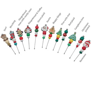 May include: A collection of Christmas-themed decorative skewers. Each skewer features a different design, including a deer, stocking, gingerbread man, Santa, and snowman. The skewers have colorful beads and festive charms.
