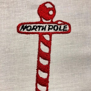 Pode incluir: Um sinal em forma de bengala de caramelo vermelho e branco com as palavras "NORTH POLE" nele.