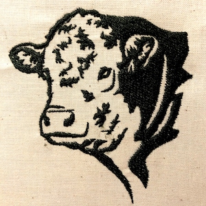 May include: Black and white embroidered image of a cow's head. The cow is facing to the left and has a spotted pattern on its face.