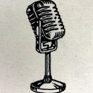 May include: Black embroidered vintage microphone on a cream-colored fabric. The microphone is detailed with a classic design, including a stand and base. The embroidery creates a textured effect, perfect for music and podcasting enthusiasts.