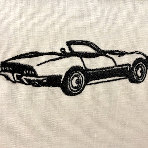 May include: Black and white embroidered image of a classic convertible sports car on a white fabric background.