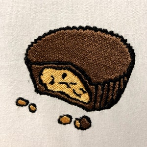 May include: A brown chocolate cup with a peanut butter filling, broken open with some peanut pieces scattered around it.