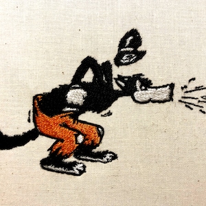 Può includere: Immagine ricamata di un lupo nero che indossa pantaloni arancioni, che soffia un soffio d'aria dalla sua bocca. Il lupo è in stile cartone animato e ha una faccia bianca.