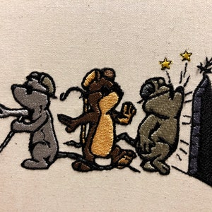Puede incluir: Diseño bordado de tres animales de dibujos animados, un ratón gris con un bastón, un ratón marrón y dorado, y un ratón gris, caminando hacia una roca negra con dos estrellas doradas encima.