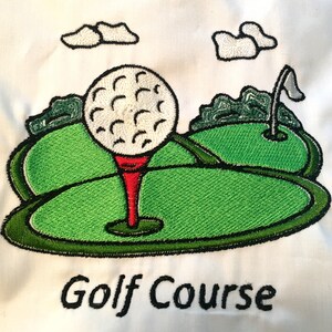 Könnte beinhalten: Gestickte Darstellung eines Golfplatzes mit einem Golfball auf einem Abschlag, grünem Gras und Wolken. Der Text "Golf Course" befindet sich unterhalb der Darstellung.