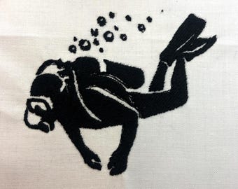 May include: Black embroidered image of a scuba diver with bubbles rising. The diver is wearing a diving mask, fins, and a tank. The image is on a white background, and the diver is angled diagonally.