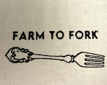 May include: Cream-colored fabric with the embroidered phrase "FARM TO FORK" above a detailed black fork design. The fork has an ornate handle and four tines, suggesting a culinary or kitchen theme.