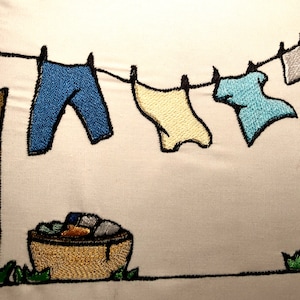 Puede incluir: Imagen bordada de ropa tendida en un tendedero. Pantalones azules, una camisa amarilla y una camisa azul claro están sujetas a la cuerda. Una cesta tejida llena de ropa está debajo. Los postes son marrones.