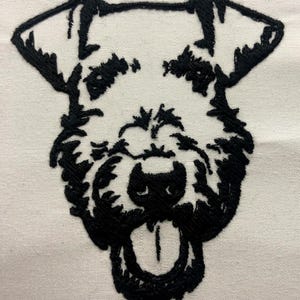 以下が含まれることがあります： 舌を出した犬の白黒刺繍画像。犬はふわふわとしたもじゃもじゃした外観をしています。