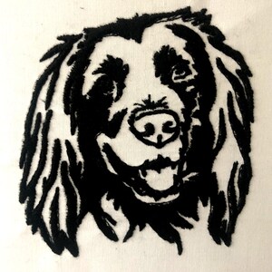 May include: A black and white embroidered image of a dog's face. The dog has long, shaggy fur and a friendly expression. The embroidery is detailed, with visible stitching creating the dog's features.