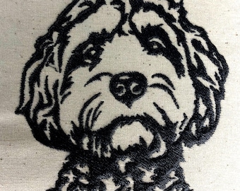 May include: Embroidered image of a dog's face in black thread on a beige fabric. The dog has a fluffy appearance with detailed stitching outlining the eyes, nose, and mouth. The design is centered and fills the frame, showcasing the dog's features.