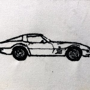 May include: Black embroidered image of a classic sports car on a white background. The car is a coupe with a low profile, visible wheels, and detailed stitching. The design is a side profile of the vehicle.