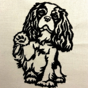 May include: Black and white embroidered image of a Cavalier King Charles Spaniel dog with long, flowing ears. The dog is standing with its front paw raised.