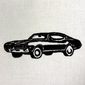 May include: Black embroidered classic car design on a white background. The car is a coupe with visible details like the headlights, wheels, and windows. The embroidery has a textured appearance, creating a vintage aesthetic.