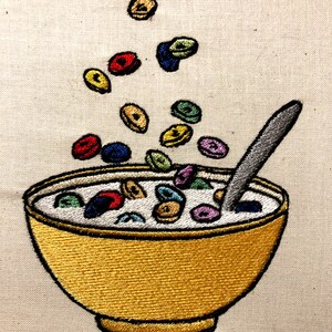 May include: A yellow bowl filled with colorful cereal and milk, with a spoon sticking out of the bowl.  There are several pieces of cereal floating in the air above the bowl.