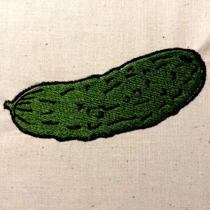 May include: A green embroidered pickle on a white fabric background.