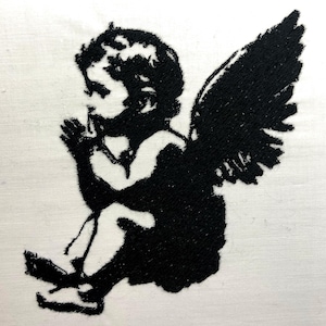 Pode incluir: Imagem bordada em preto e branco de um querubim com asas, rezando com as mãos juntas.