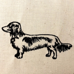 May include: Black and white embroidered image of a dachshund dog on a beige fabric background.