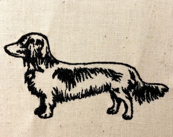 May include: Black and white embroidered image of a dachshund dog on a beige fabric background.