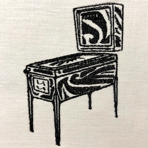 May include: Black and white embroidered image of a vintage pinball machine with a raised glass panel. The machine has a wood grain design.