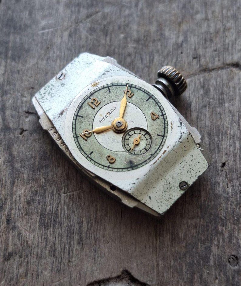 Peut inclure: Montre-bracelet vintage avec un bo&icirc;tier argent&eacute; vieilli et un cadran vert d&eacute;lav&eacute;. Le cadran pr&eacute;sente des aiguilles et des chiffres dor&eacute;s, avec un petit cadran secondaire. La montre est partiellement d&eacute;mont&eacute;e, montrant des signes d'&acirc;ge.