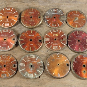 Puede incluir: Una colección de esferas de reloj vintage en tonos naranja y rojo, con números y manecillas blancas. Las esferas muestran varias marcas y los números 12, 9, 6 y 3. Las esferas son redondas y muestran signos de desgaste.