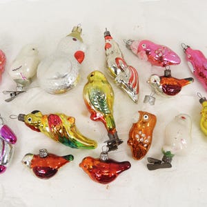 Puede incluir: Una colección de adornos de pájaros de vidrio vintage en varios colores, incluyendo rosa, blanco, amarillo, verde, naranja y rojo. Los adornos tienen la forma de diferentes pájaros, como un gallo, un loro y un pollito.