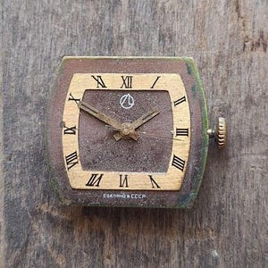 Peut inclure: Cadran de montre carr&eacute; vintage avec un cadran marron, des chiffres romains dor&eacute;s et des aiguilles dor&eacute;es. Le cadran de la montre a un cadre dor&eacute; et une couronne de remontoir sur le c&ocirc;t&eacute;. Le texte "СДЕЛАНО В СССР" est imprim&eacute; en bas.
