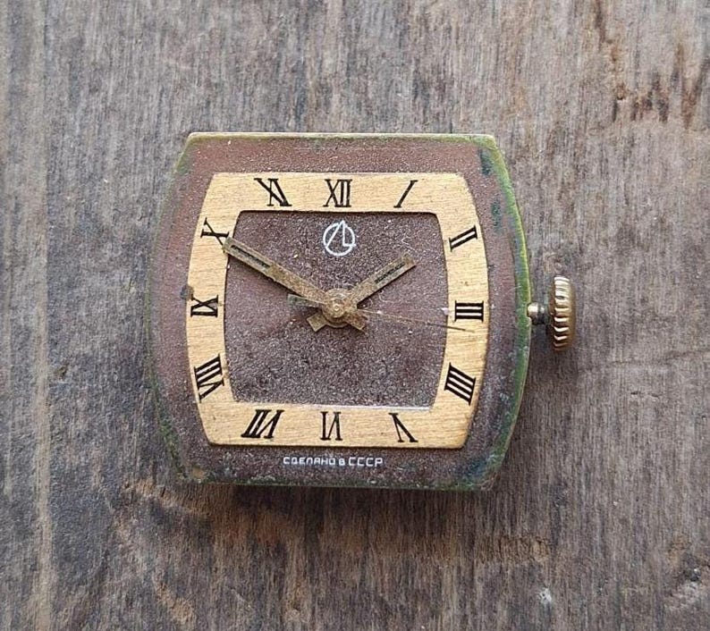 Peut inclure: Cadran de montre carr&eacute; vintage avec un cadran marron, des chiffres romains dor&eacute;s et des aiguilles dor&eacute;es. Le cadran de la montre a un cadre dor&eacute; et une couronne de remontoir sur le c&ocirc;t&eacute;. Le texte "СДЕЛАНО В СССР" est imprim&eacute; en bas.