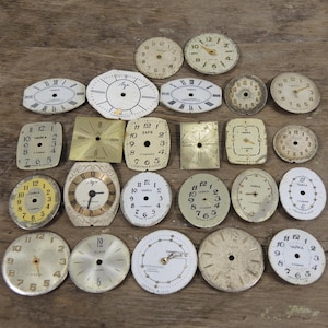 Könnte beinhalten: Eine Sammlung von Vintage-Zifferblättern in verschiedenen Formen und Größen, darunter rund, oval und quadratisch. Die Zifferblätter sind hauptsächlich weiß, cremefarben und goldfarben, mit schwarzen Ziffern und Zeigern. Einige Zifferblätter haben Text, einschließlich des Wortes "ЧАЙКА".