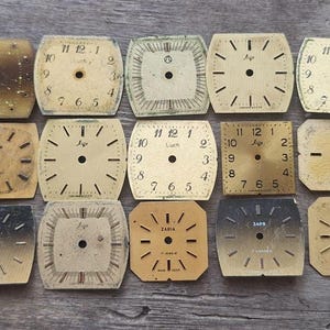 Op de afbeelding: Een verzameling van vijftien vintage horlogefaces in verschillende vormen en tinten beige en bruin. Elk gezicht heeft een centraal gat en markeringen voor de uren, sommige tonen de merknamen "Luch" en "Zaria".