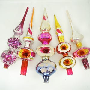 Op de afbeelding: Vijf vintage glazen kerstboompieken met langwerpige punten en bolvormige middendelen. Elk ornament is voorzien van unieke handgeschilderde bloemmotieven, reflecterende metallic afwerkingen en levendige kleuren zoals magenta, goud, zilver en blauw.