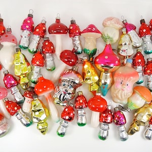 Puede incluir: Una colección de adornos navideños de vidrio vintage con forma de champiñones. Los adornos son de varios colores, incluyendo rojo, verde, blanco y amarillo. Algunos de los adornos tienen detalles pintados, como puntos blancos y una cara sonriente.