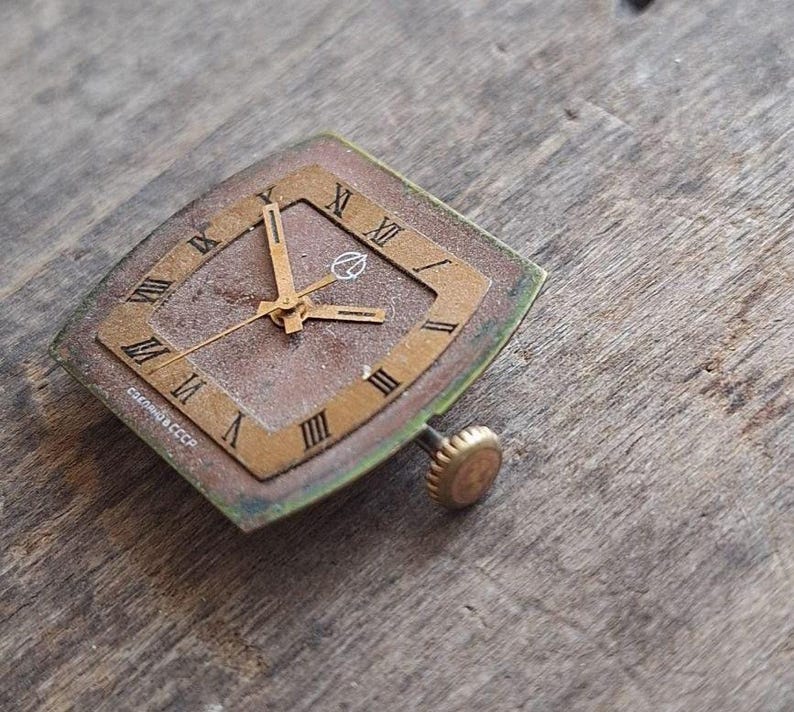 Peut inclure: Cadran de montre vintage de forme carr&eacute;e en losange. Il pr&eacute;sente des chiffres romains, des aiguilles dor&eacute;es et un petit logo. Le cadran a un cadre dor&eacute; et un cadran marron. Le texte "Сделано в СССР" est visible.