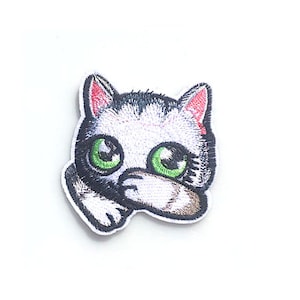 May include: Embroidered iron-on patch featuring a cartoon cat with large green eyes, black and white fur, and pink ears. The cat is looking to the left and has its paw covering its face.