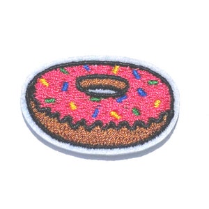 May include: A pink donut with colorful sprinkles and a brown glaze. The donut is embroidered on a white fabric patch.