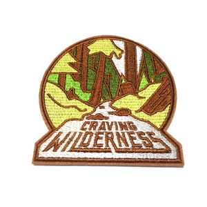 May include: Brown and green embroidered patch with a forest scene and the text "Craving Wilderness".