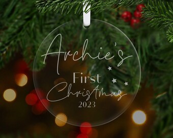 Könnte beinhalten: Runder, transparenter Weihnachtsbaumschmuck mit dem Text "Archie's First Christmas 2023" in weißer Schrift.