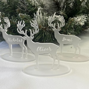 May include: Three white acrylic reindeer place card holders with the names "Nicholas", "Oliver", and "Domi" engraved on them.
