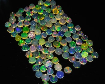 Puede incluir: Una colección de cabujones de ópalo iridiscente en varios tonos de verde, azul y amarillo. Los cabujones son redondos y tienen una superficie lisa y pulida.